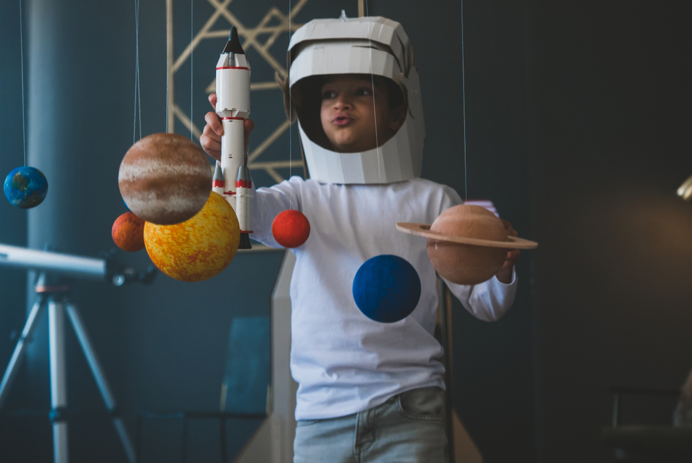 Photo of a young child dressed in space suit playing with planets at Space Center Houston. 