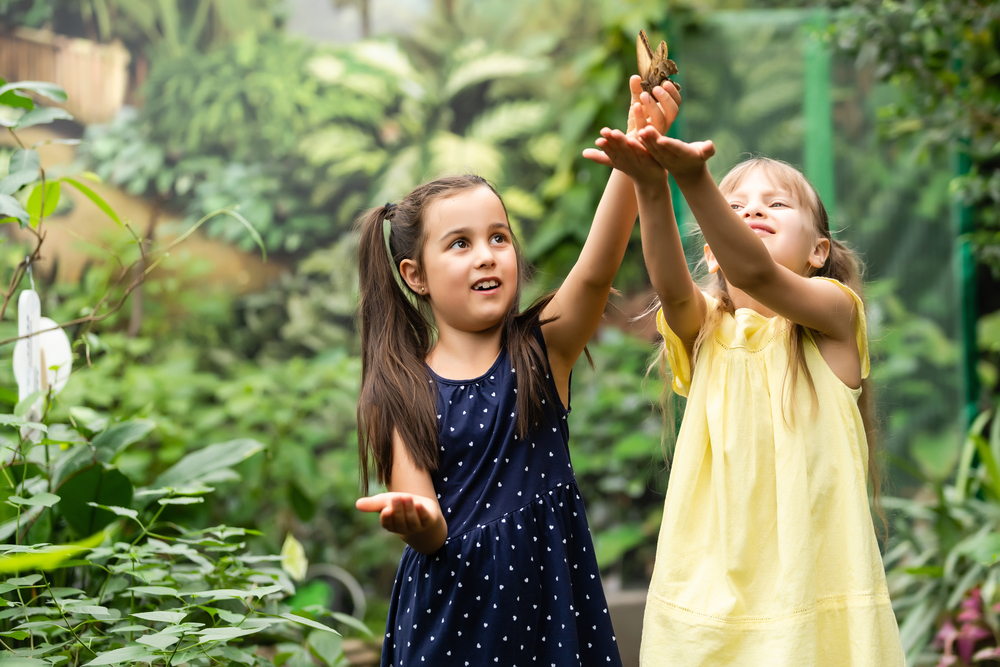 Two girls holding up their hands for a butterfly to land on at the Cockrell Butterfly Center. 
