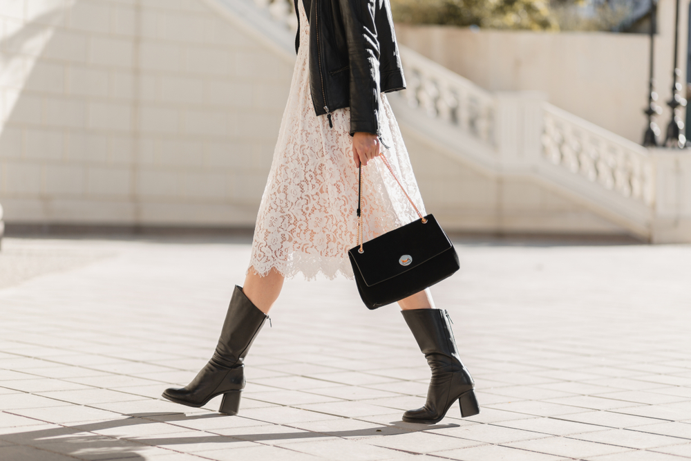 Waist down photo of a woman wearing a lacy white dress, leather jacket, and boots, one of the great Austin Outfit Ideas.