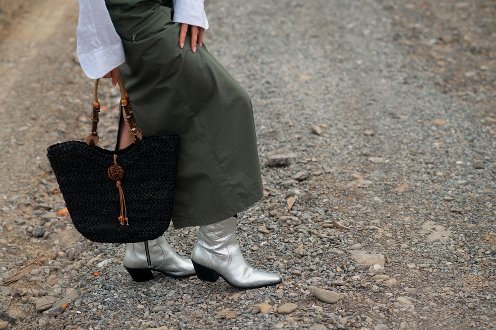  Black straw wicker bag, purse, maxi green skirt, silver cowboy boots in trendy outfit. Woman posing outdoor.  Dallas outfit ideas for shoes