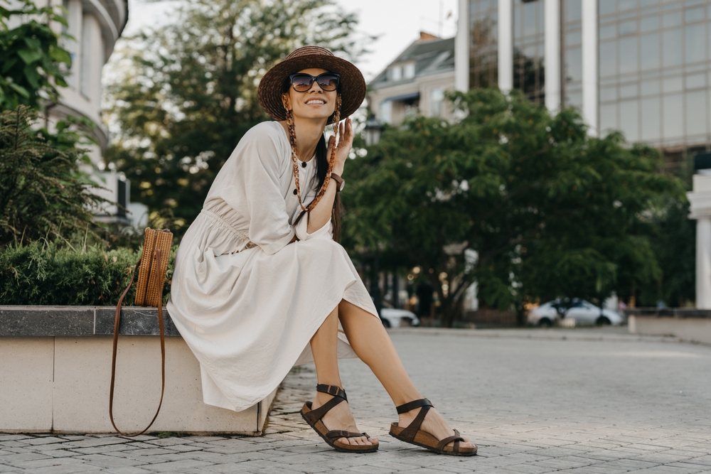 woman walking in street on vacation dressed in white summer fashion dress straw hat sunglasses and purse, smiling happy having fun, stylish