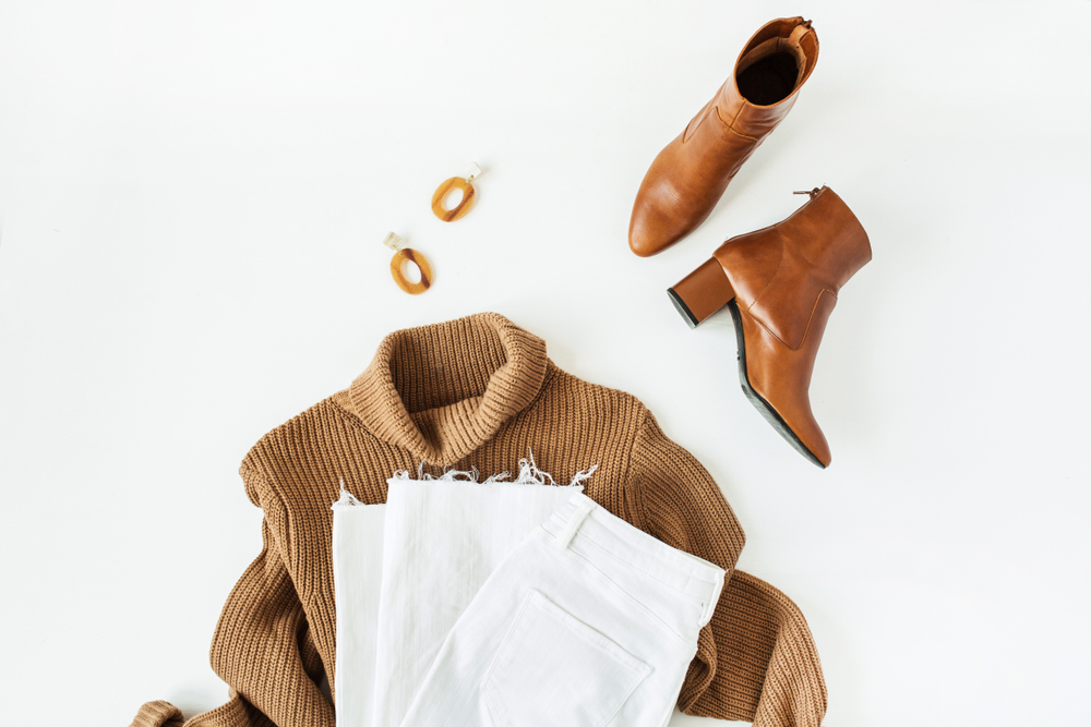 Flat lay fashion collage with women modern clothes and accessories on white background. Brown turtleneck pullover, shoes, jeans, earrings. 