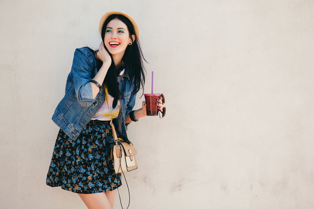  hipster girl, cocktail, smoozy drink, denim jacket, smiling, fashion, teen, cool accessories, purse, hat, sunglasses. The article is about what to wear in Houston