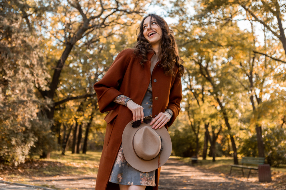 close-up hands details of attractive stylish woman holding hat and sunglasses walking in park dressed in warm coat autumn trendy street fashion style accessories