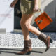 A woman knows she fits right in San Antonio as she walks down the street with an orange clutch, cowboy boots, and a tweed jacket on that extends past her shorts.